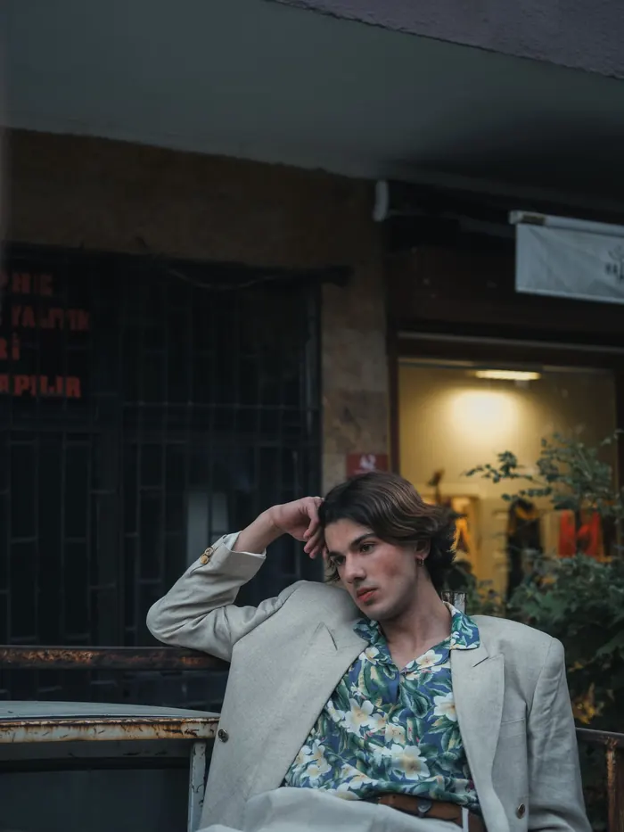 Jeune homme en blazer clair et chemise fleurie assis en ville