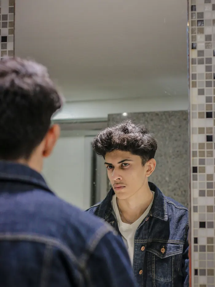 Jeune homme en veste en jean qui se regarde dans un miroir