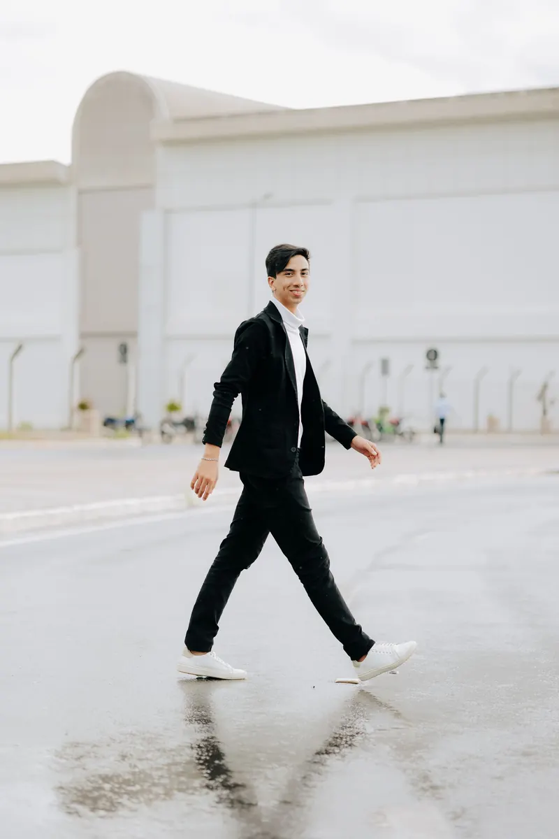 Jeune homme mince en costume noir ajusté traversant une place