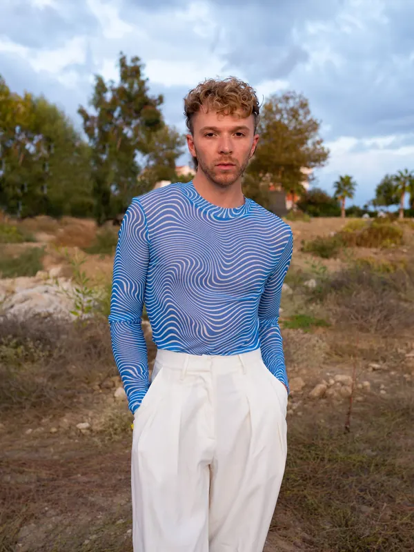 Jeune homme mince en haut moulant bleu imprimé et pantalon blanc à pinces en extérieur