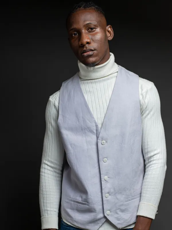 Jeune homme élancé en col roulé blanc et gilet de costume gris sur fond sombre
