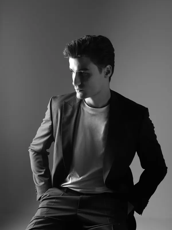 Photo noir et blanc d’un jeune homme mince en blazer et t-shirt sous un éclairage latéral marqué