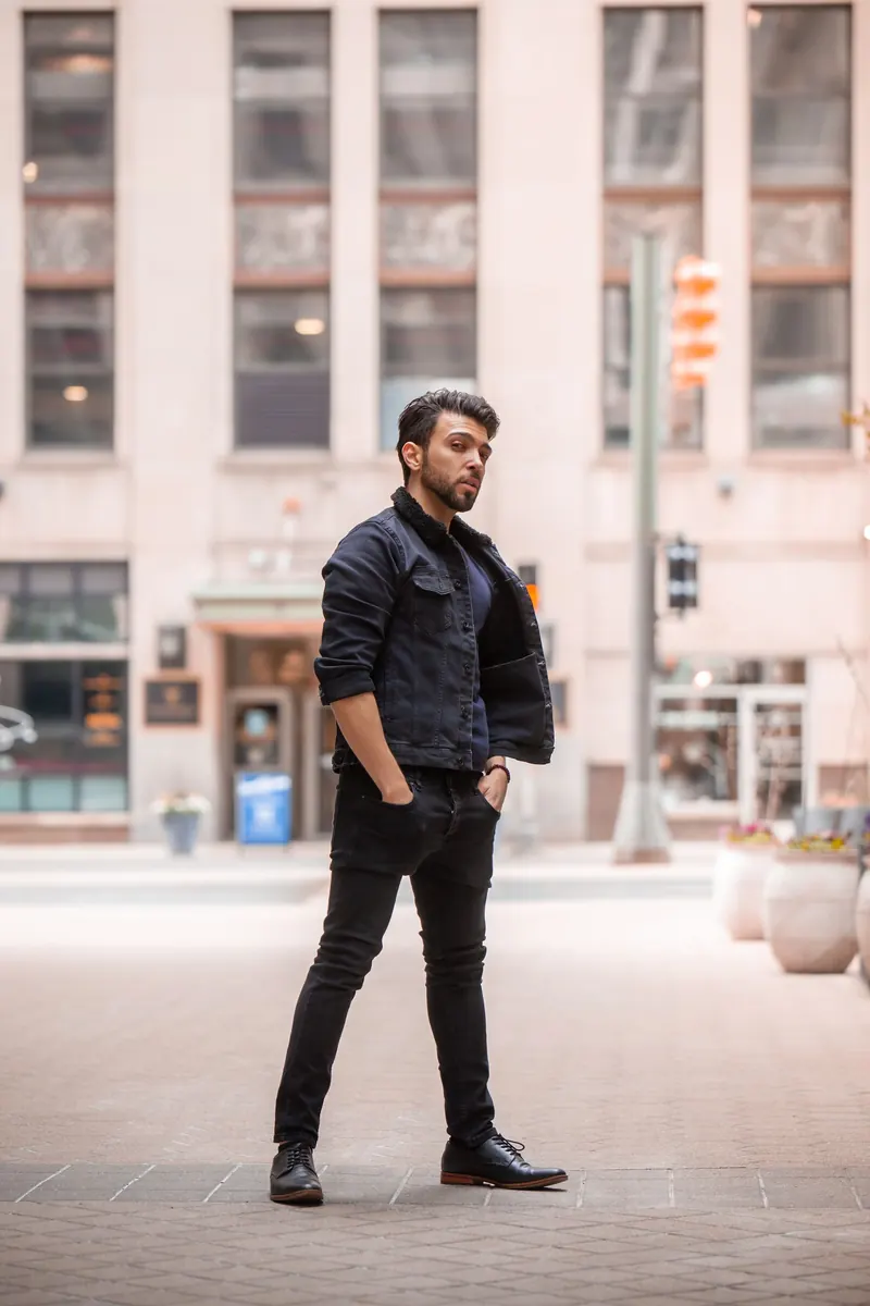 Slim young man in black skinny jeans and a dark jacket on a city plaza
