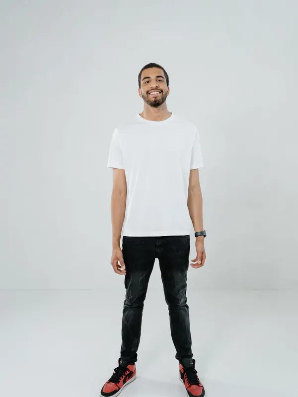 Jeune homme mince en t-shirt blanc et jean noir skinny contre un mur de studio blanc
